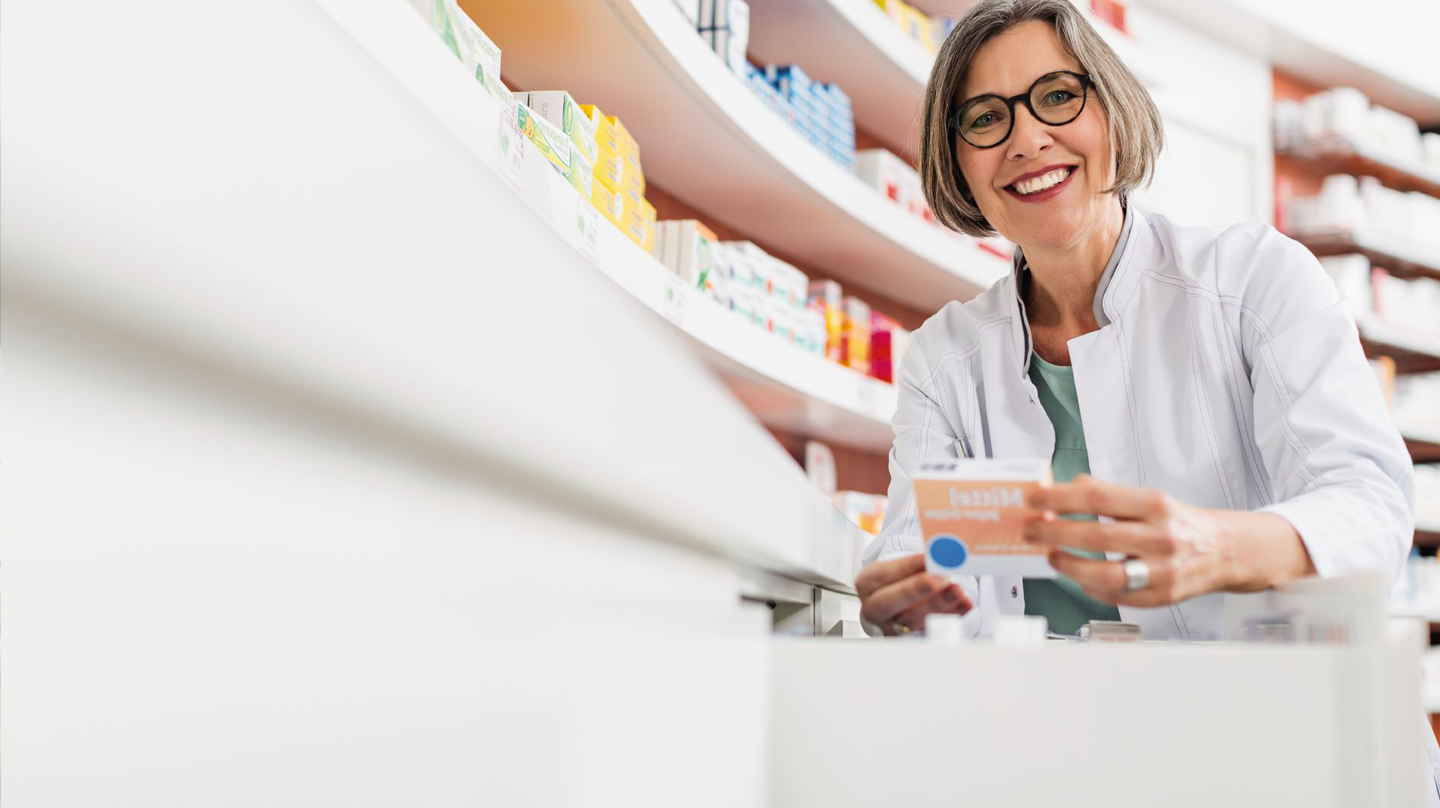 Arzneimittelsicherheit: Apothekerin vor Regal mit Medikamenten hält eine Medikamentenpackung in der Hand.